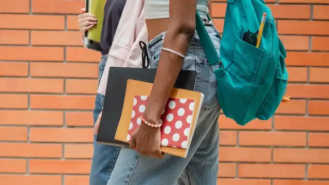 Dois estudantes caminhando com mochila, pastas e cadernos em um campus